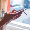 Une jeune femme tape sur un téléphone intelligent en fumant une cigarette.