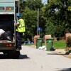 Un homme est sur le marchepied d'un camion qui collecte les poubelles.