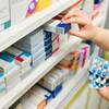 Un pharmacien place des boites de pilules sur une étagère.