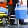 Un ambulancier porte une glacière bleue pour un don d'organes. Une civière se trouve en avant-plan.