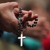 Les mains jointes, une personne tient un chapelet avec une croix bien visible au bout de la chaîne.