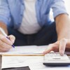 Un homme fait un budget avec une calculatrice, crayon et papier.