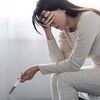 Sous le choc, une femme en pyjama est assise sur le bord de son lit, le front appuyé sur une main. Elle tient un test de grossesse autoadministré.