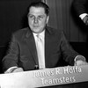 Photo en noir et blanc d'un homme assis devant une affiche avec l'inscription James R. Hoffa Teamsters.