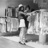 Deux femmes en minijupe sourient en fouillant dans des vêtements dans un magasin.