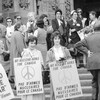 Des femmes manifestent tandis que trois hommes circulent devant elles sans les regarder; deux d'entre elles tiennent une pancarte sur laquelle avec l'inscription pas d'armes nucléaires pour le Canada.