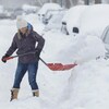 Une femme pellette la neige pour dégager sa voiture dans une rue de Montréal.