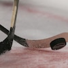 Deux bâtons de hockey et une rondelle, lors d'une mise au jeu. 