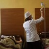 Une femme ajuste un soluté administré à un homme couché sur un lit. 