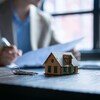Clés et maison sur la table devant un individu signant des papiers.