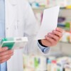 Un pharmacien tient dans une main une boîte de médicaments et dans l'autre une prescription.