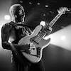Josh McLeod joue une basse sur scène et la photo est en noir et blanc.