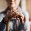 Une personne âgée tient une canne de ses deux mains.