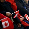 Des personnes sont assises et tiennent dans leurs mains un drapeau canadien.