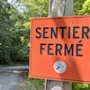 Un panneau orange indique que le sentier est fermé.