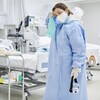 Une travailleuse de la santé fatiguée, vêtue d'une combinaison de protection, essuie la sueur sur son front dans une salle d'hôpital. 