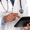 Un médecin photographié des épaules à la taille, tient une tablette dans ses mains.