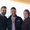 P-A Méthot, humoriste et animateur sourit en compagnie d'une femme à sa gauche et d'un homme à sa droite sur un balcon intérieur de la Nouvelle Maison de Radio-Canada. 