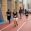 Trois personnes qui courent sur une piste intérieure  et un caméraman derrière.