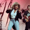 Tina Turner en mouvement sur scène, un microphone à la main.