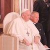 Le pape est assis et à ses côtés, se retrouve un prêtre
