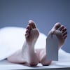 Photo des pieds d'une personne allongée sur une table recouverte d'un drap, avec une étiquette au pied.