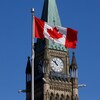 Un drapeau canadien flotte devant la tour du parlement fédéral. 
