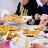 Des personnes rassemblées autour d'une table sur laquelle se trouve plusieurs plats de viande, de feuilletés et de fruits séchés.
