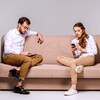 Un homme et une femme assis sur un divan consultent chacun leur cellulaire.