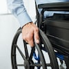 La main d'une personne en fauteuil roulant posée sur la roue.