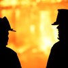Silhouette de deux pompiers dans une lumière jaune orangé qui évoque un incendie.