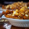Gros plan sur un plat composé de frite, de fromage en grains et de sauce brune, sur une table. 