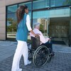 Une femme pousse le fauteuil roulant d'un homme à l'entrée d'un édifice.