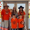 Trois femmes et trois enfants portant des chandails orange posent pour une photo.