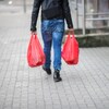 Un homme vu de dos porte des sacs en plastique en marchant sur le trottoir. 