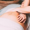 Deux mains de femme sur le ventre d'une femme enceinte couchée sur le dos.