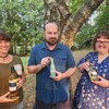 Trois personnes devant un arbre, tenant dans leurs mains chacun une bouteille de vin.