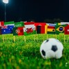Des drapeaux des pays participant à la Coupe du monde et un ballon sur un terrain de soccer.