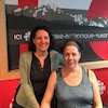 Deux femmes  souriantes aux cheveux foncés dans un studio d'enregistrement. Celle de gauche est debout et tient par l'épaule l'autre femme qui est assise.