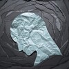 Image conceptuelle d'une émotion négative : un silhouette de tête en papier blanc froissé sur fond de papier noir déchiré.
