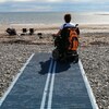 Une personne en fauteuil roulant est sur une plage grâce à un tapis au sol 
