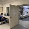 Une technologue en imagerie médicale travaille à l'ordinateur de l'autre côté d'une fenêtre qui donne accès à l'appareil d'IRM.