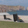 Une femme est assise sur une chaise longue sur une plage devant le rocher Percé.