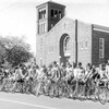 Photo noir et blanc de compétiteurs sur leurs bicyclettes à la ligne de départ d'une course.