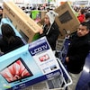 Des clients dans un magasin d'électronique attendent en file à la caisse pour payer. La plupart ont acheté une télévision.