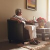 Une femme âgée assise dans un fauteuil, dans le salon d'une maison.