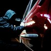 Un voleur de voiture en action tard dans la nuit, portant des vêtements noirs.