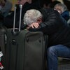 Un homme se repose sur une valise dans un aéroport.