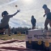 Un groupe de femmes joue au Spikeball, un jeu consistant à faire rebondir une balle sur un trampoline. Une caisse de bière Corona est installée en avant-plan. 