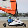 Un homme assis dans un petit véhicule à voile à trois roues sur une plage. 